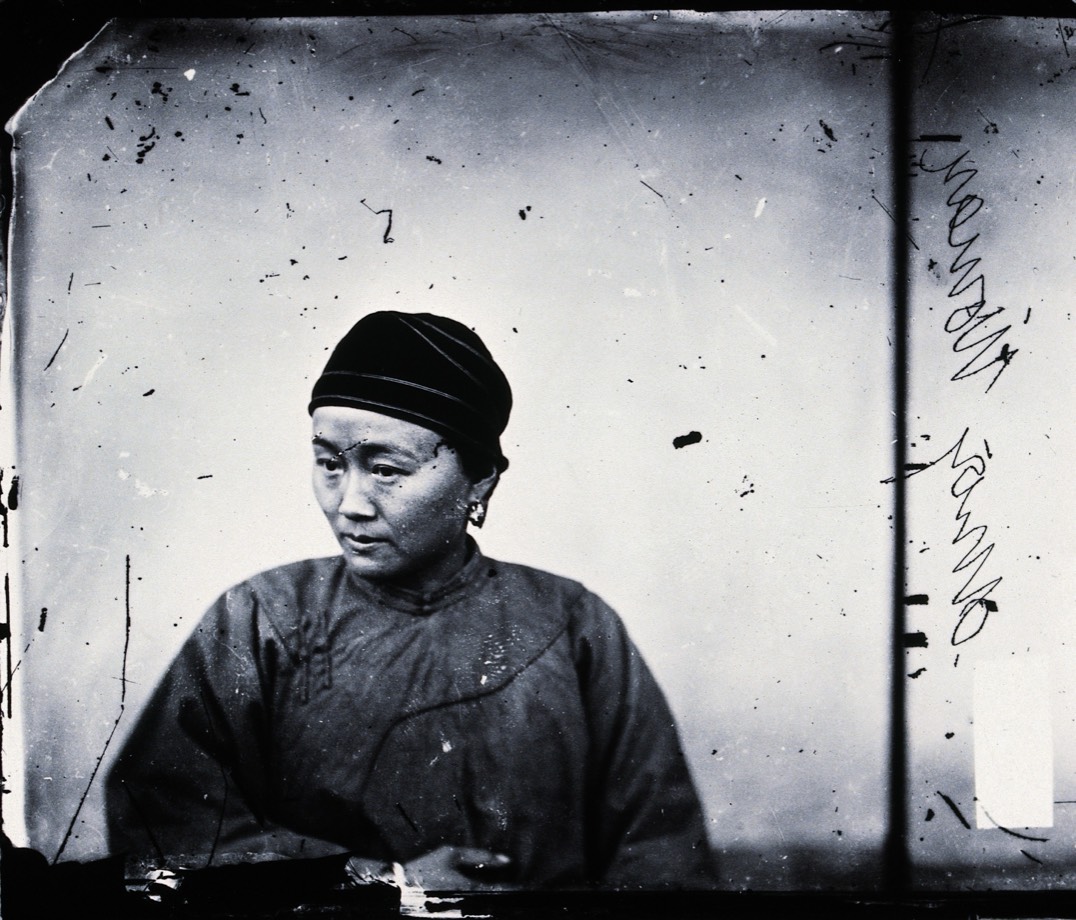 A scratched black-and-white glass-plate portrait of a seated woman in Amoy, China
