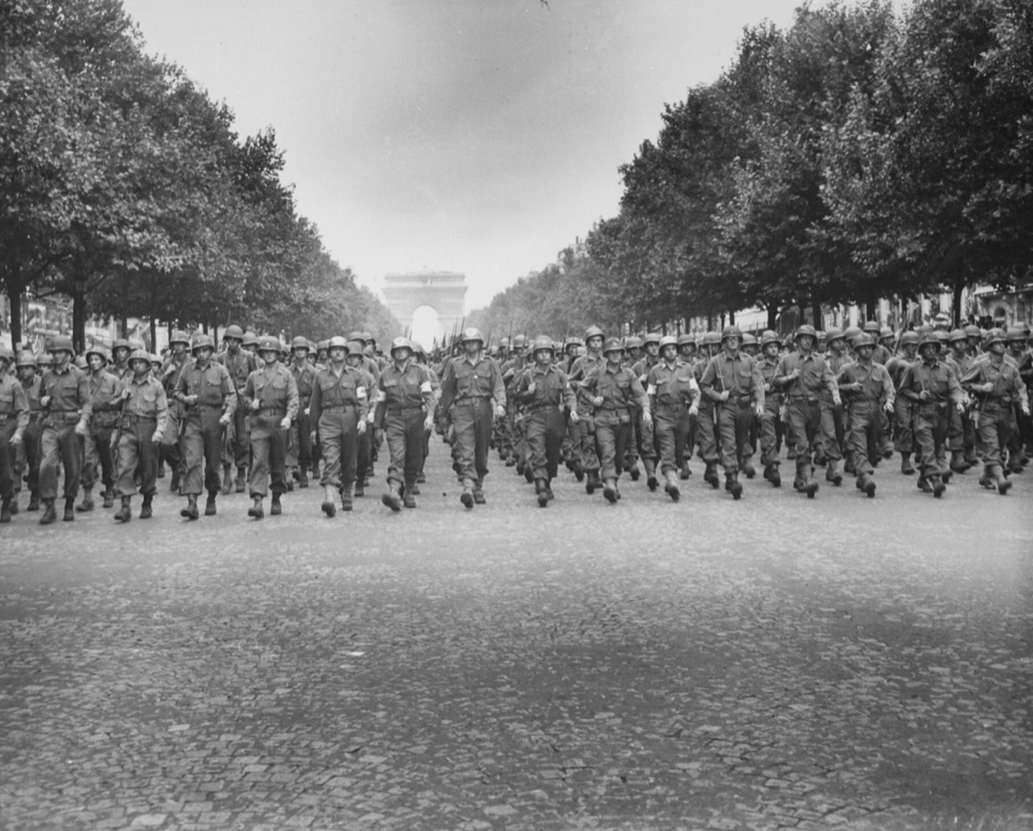 Black-and-white 1944 photograph of American troops marching 24-abreast down the Champs-Élysées toward the Arc de Triomphe